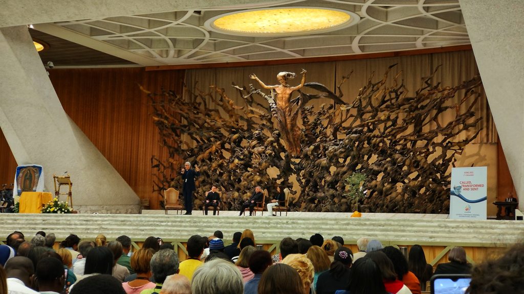 Foto: Nicky Gamble auf CHARIS-Treffen 2023 vor dem Hintergrund des auferstanderen Christus in Aula Pauls VI.